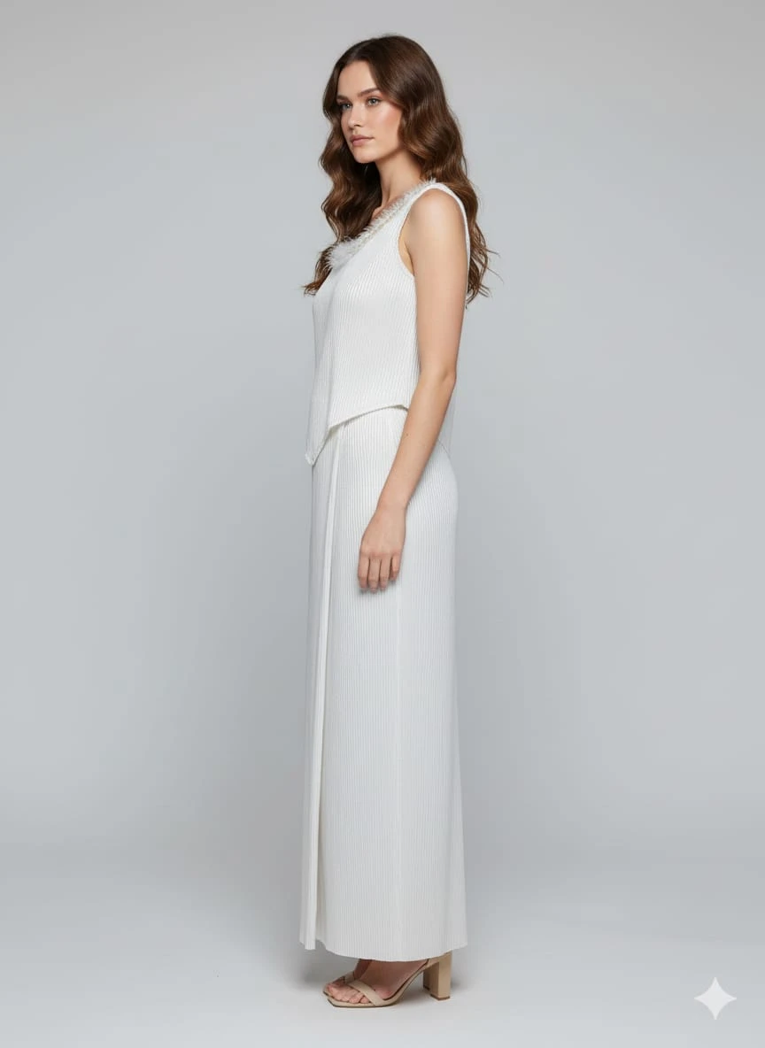 Woman wearing a white sleeveless pleated maxi dress with a layered pointed overlay and beige heels
