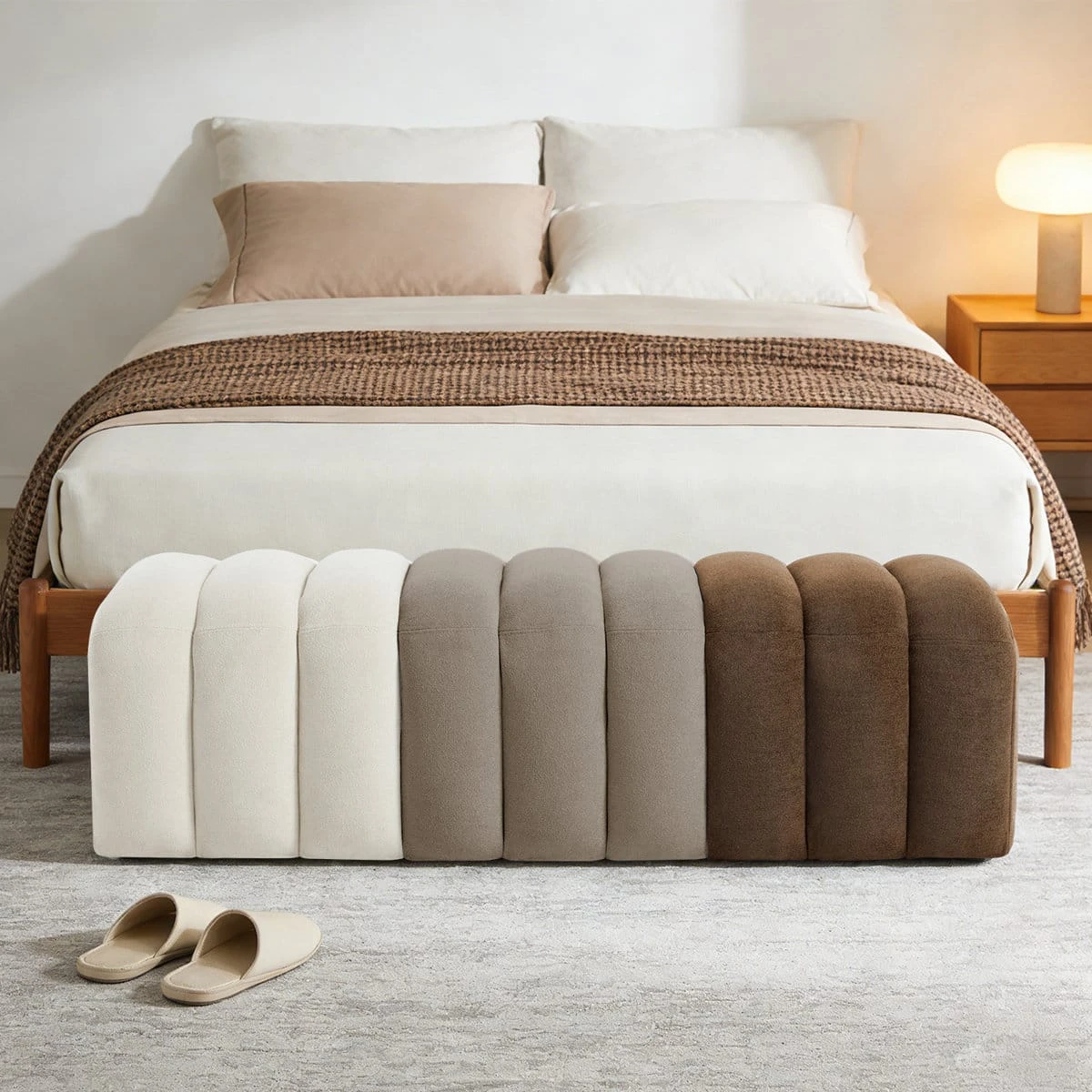 Front view of the long upholstered bench placed at the foot of a bed with cream, taupe and brown panels