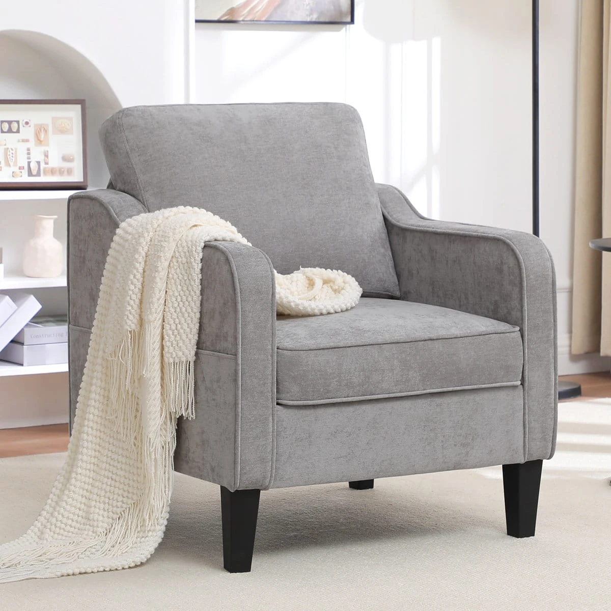 Front angled view of the grey accent chair with a cream throw draped over one arm
