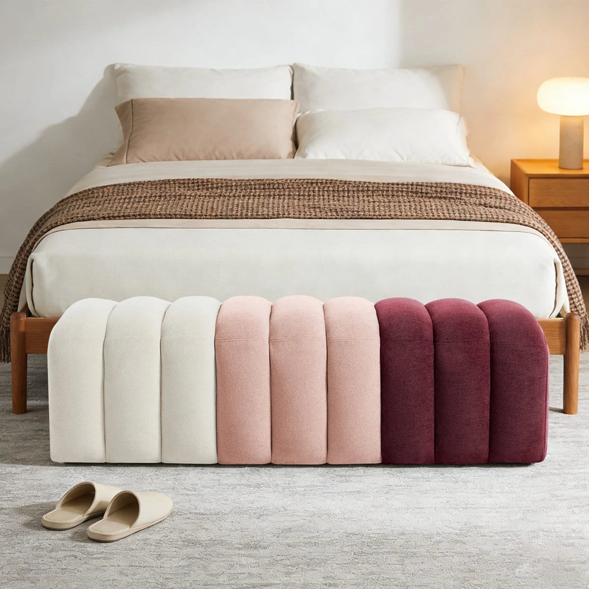 Front view of the tufted bench placed at the foot of a bed, showing its long rounded silhouette