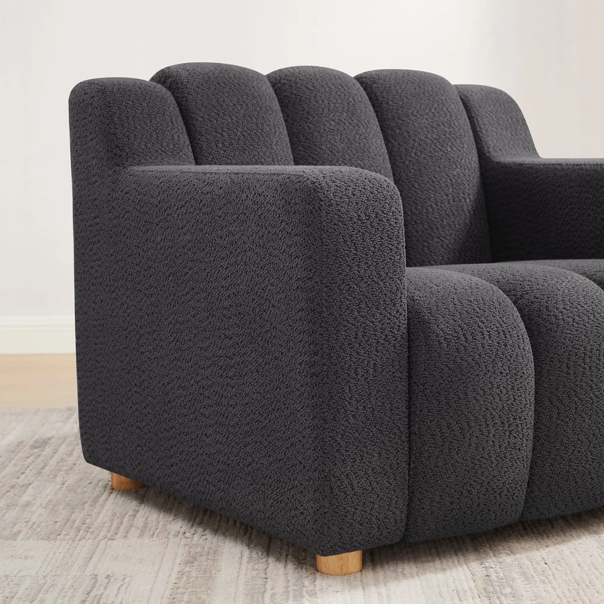 Close-up side angle showing the textured boucle upholstery, wide armrest and front wood leg
