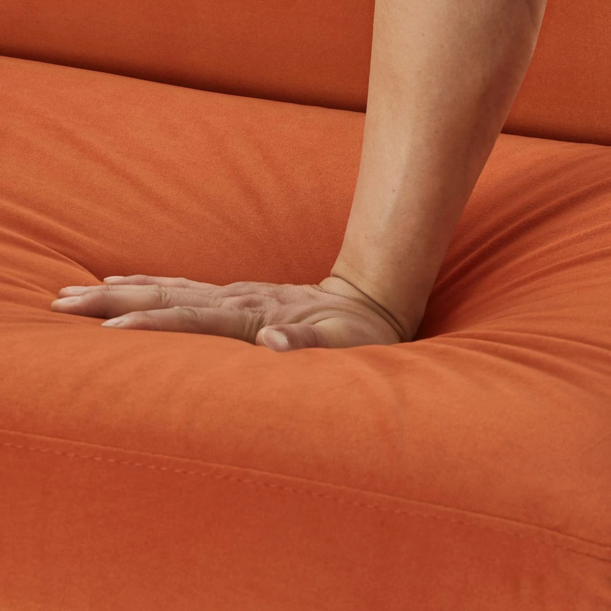 Close-up of hand pressing the orange upholstered seat cushion to show softness and padding