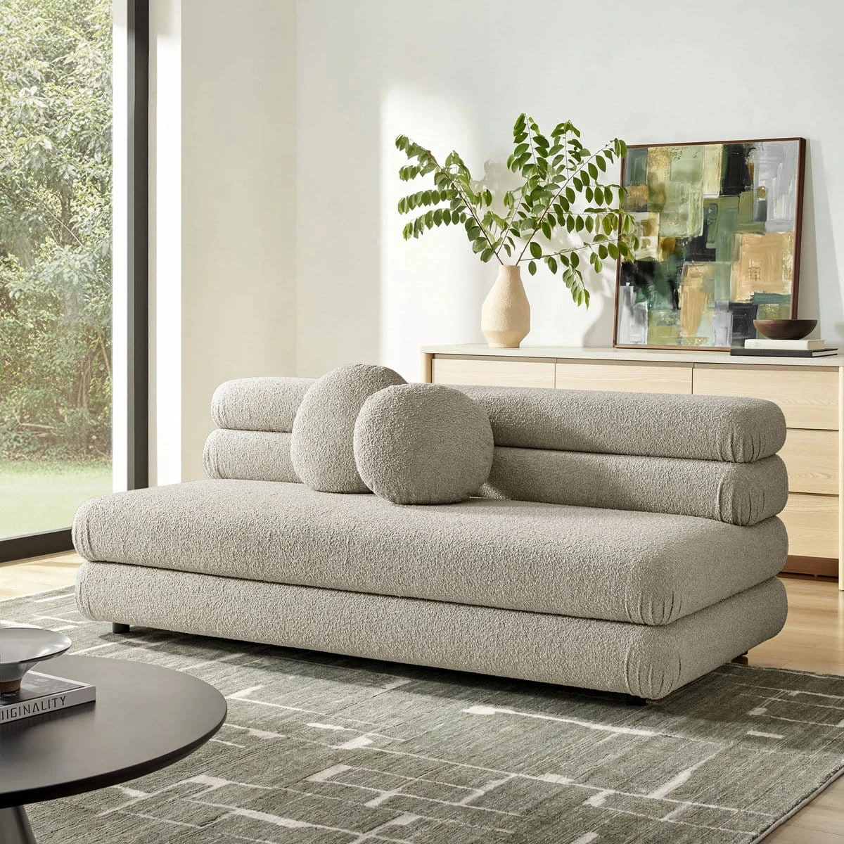 Front angled view of the cream textured sofa with twin round pillows in a bright room with abstract art