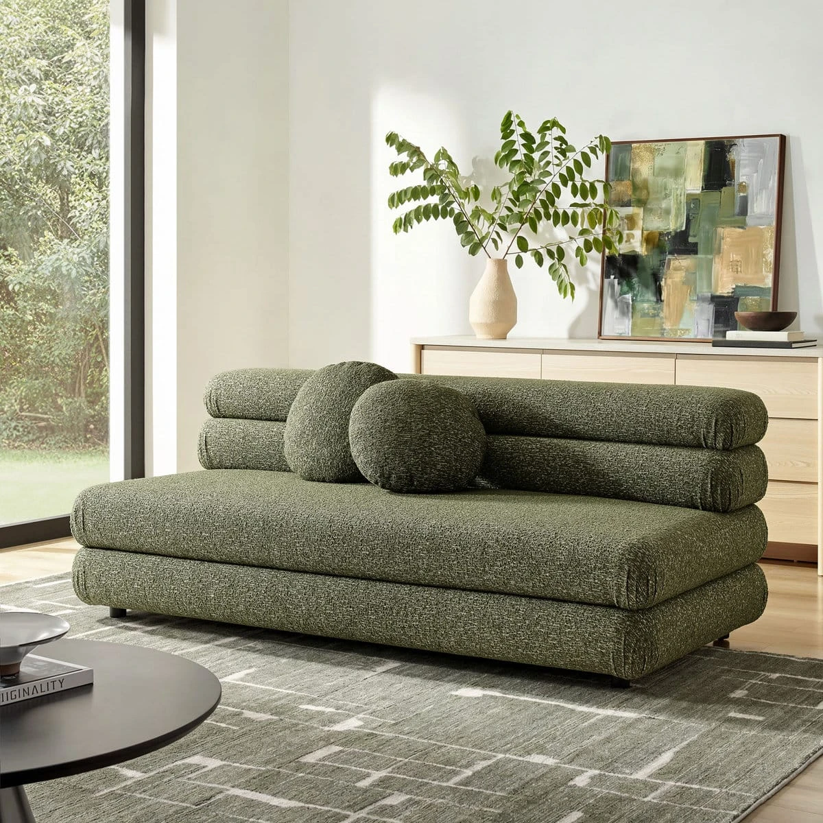 Wide room view of the olive sofa on a patterned rug beside a console and framed artwork