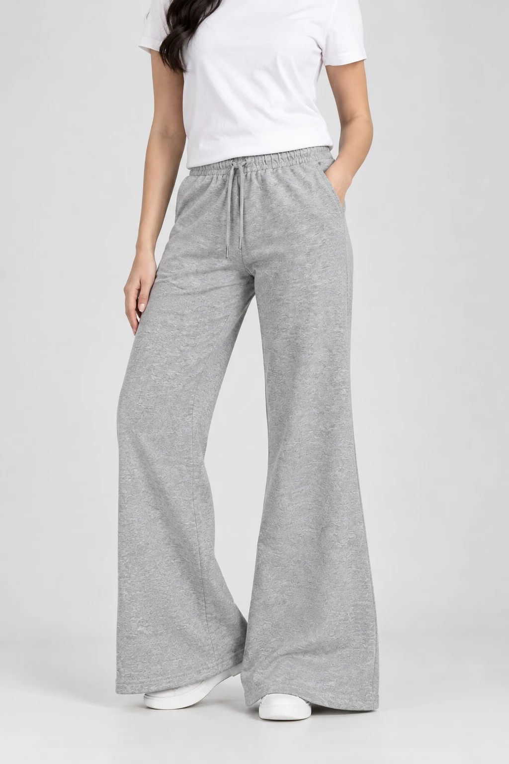 Close-up angled view of grey wide-leg lounge pants showing elastic drawstring waistband and hand in pocket
