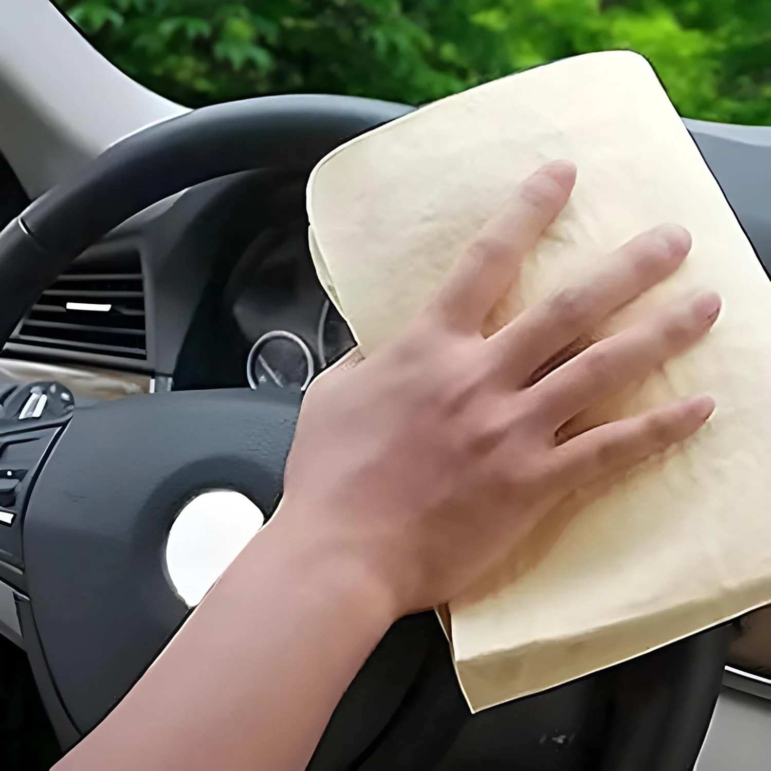 Cream shammy towel wiping a car dashboard and steering wheel in use