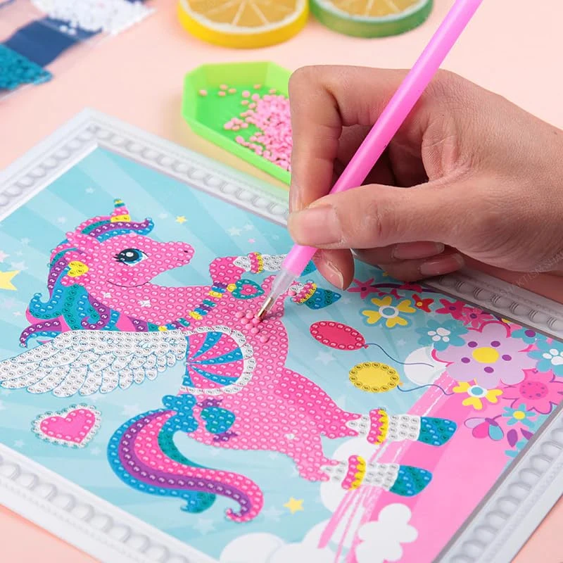 Hand placing pink gems on a framed winged unicorn diamond painting with balloons and flowers