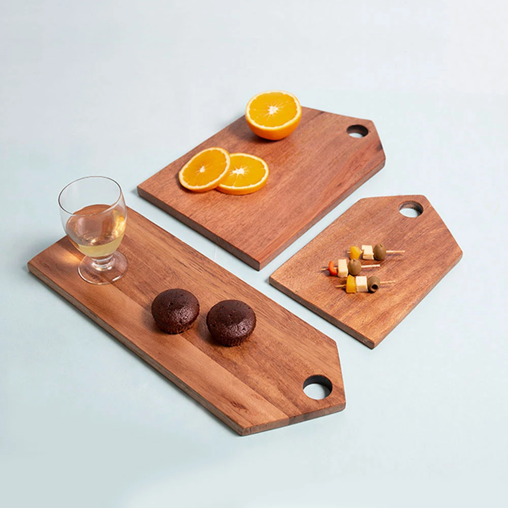 Three acacia wood serving boards styled with oranges, skewers, muffins and a glass on a light background