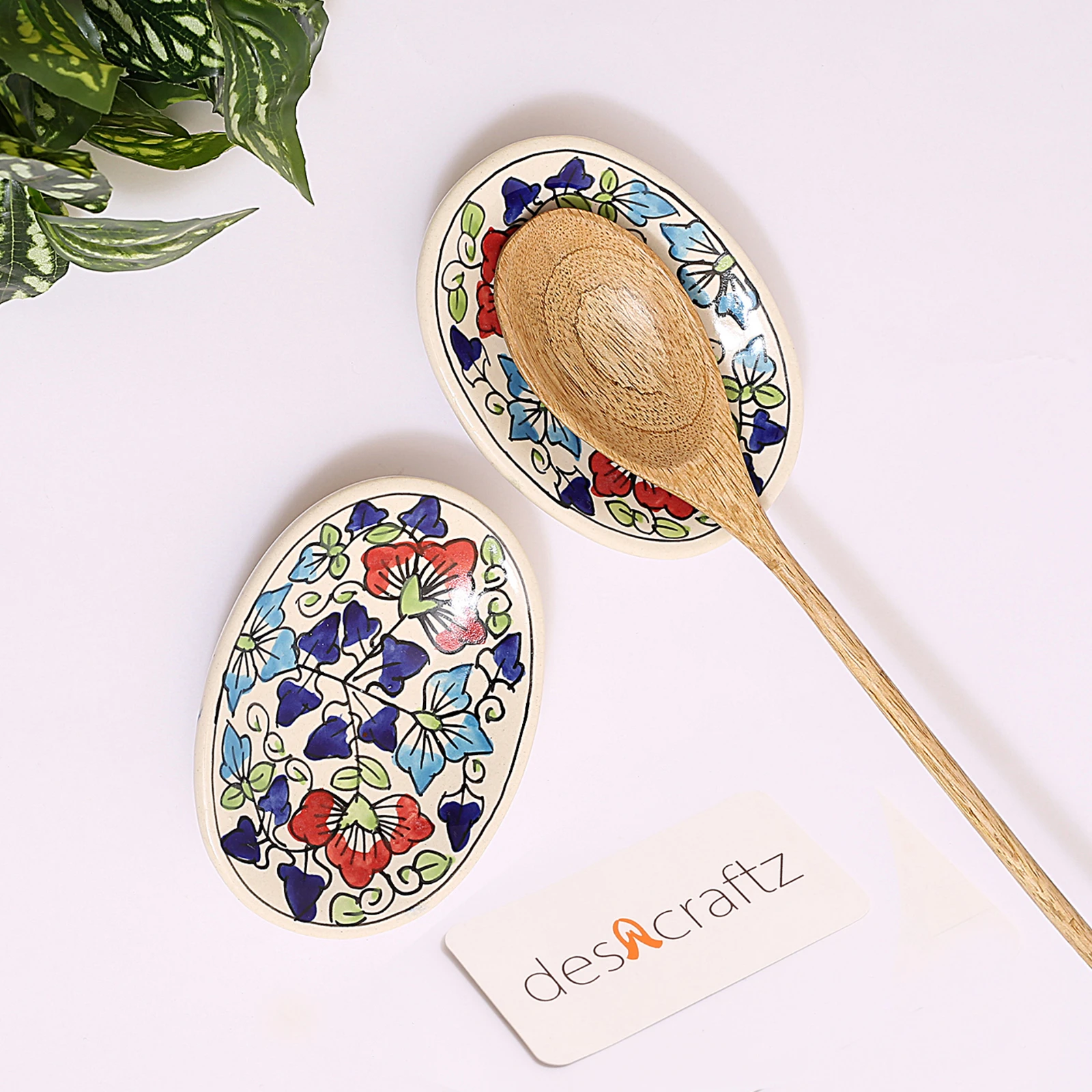 Two oval floral ceramic spoon rests displayed flat, with a wooden spoon placed on one piece. Dimension - 3.5'' x 4'' x 1''