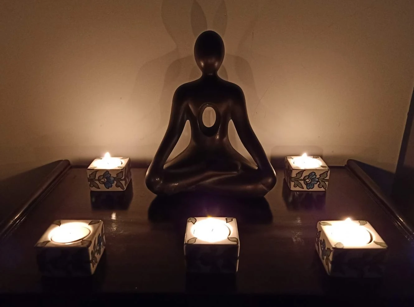Two floral tea light holders lit on a dark table around a seated meditation figurine