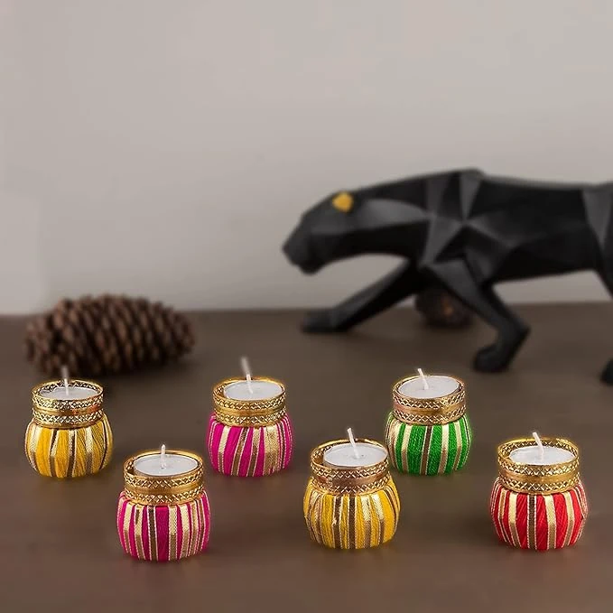 Six colorful thread-wrapped tealight holders with gold trim displayed on a wooden tabletop