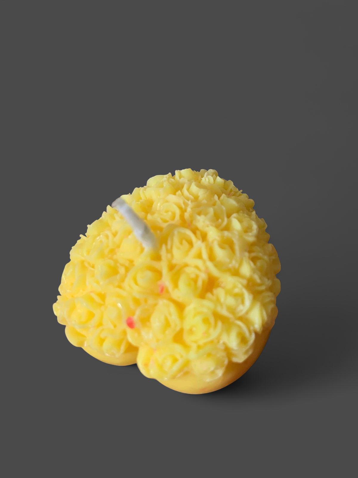 Angled close-up of a yellow heart candle with raised rose clusters and a centered white wick on maroon fabric