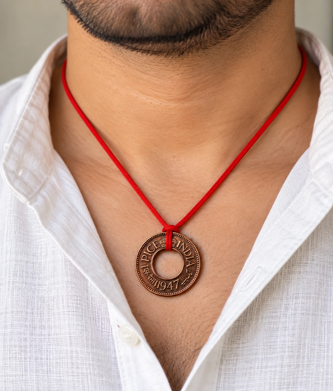 1947 India one pice coin pendant tied on a red thread necklace, worn with an open white shirt