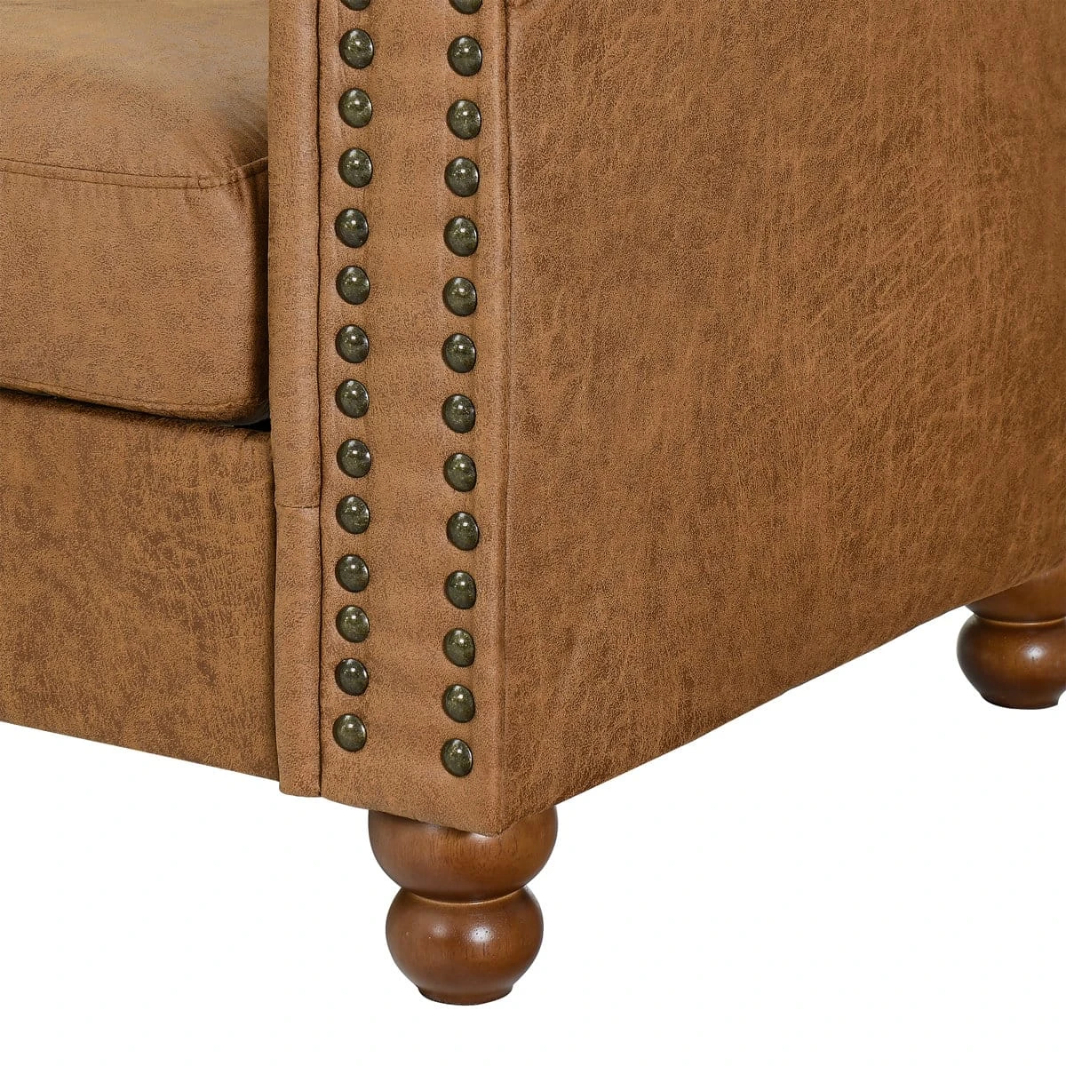 Detail of the armchair corner with antique brass nailheads, distressed tan upholstery and turned wood foot