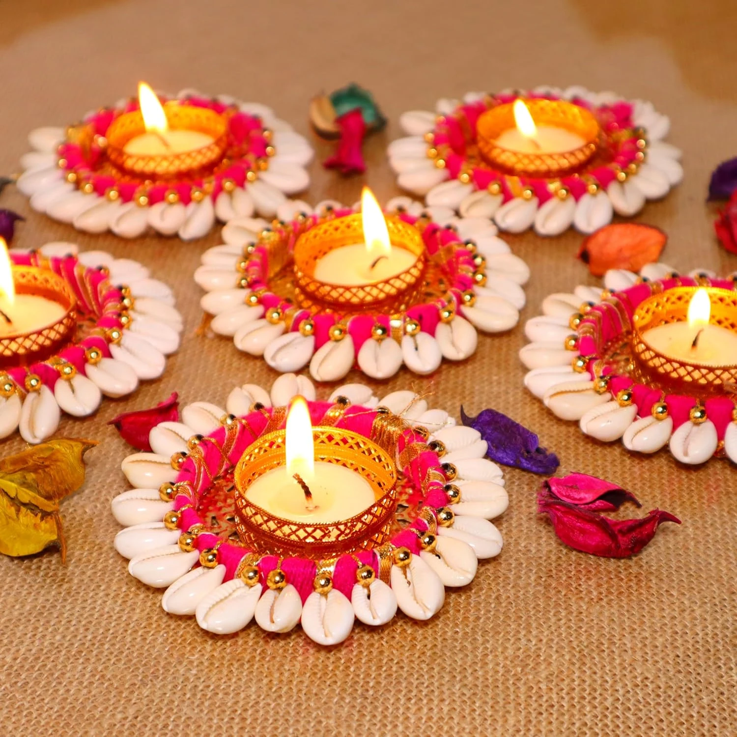 Multiple lit cowrie shell tealight holders arranged decoratively on a burlap surface