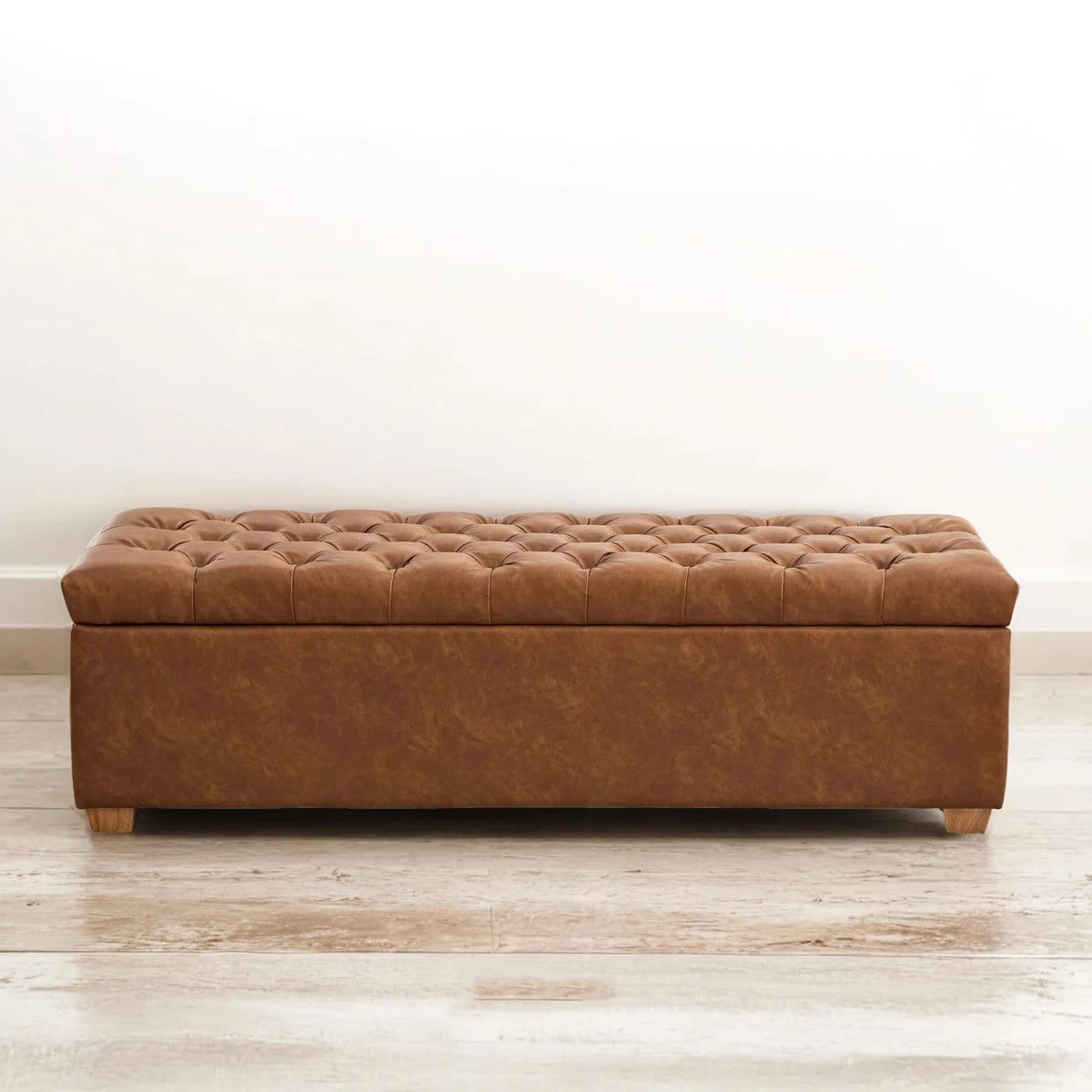 Front view of the closed tufted brown bench with wooden feet on a light floor