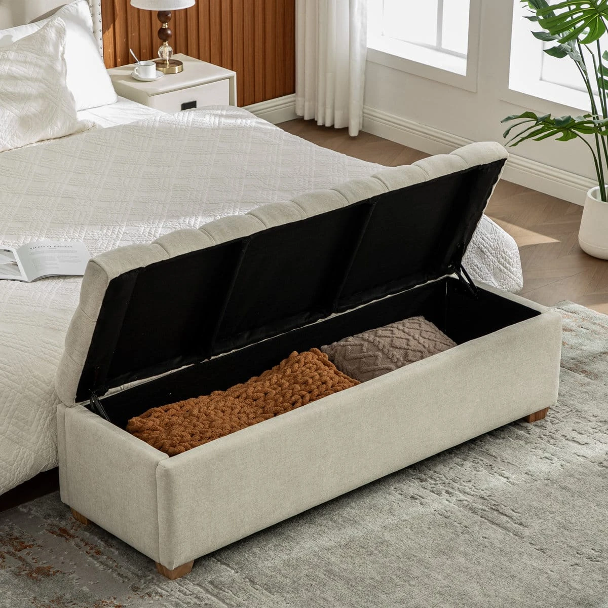 Storage bench opened beside a bed, showing blanket storage inside the black-lined compartment
