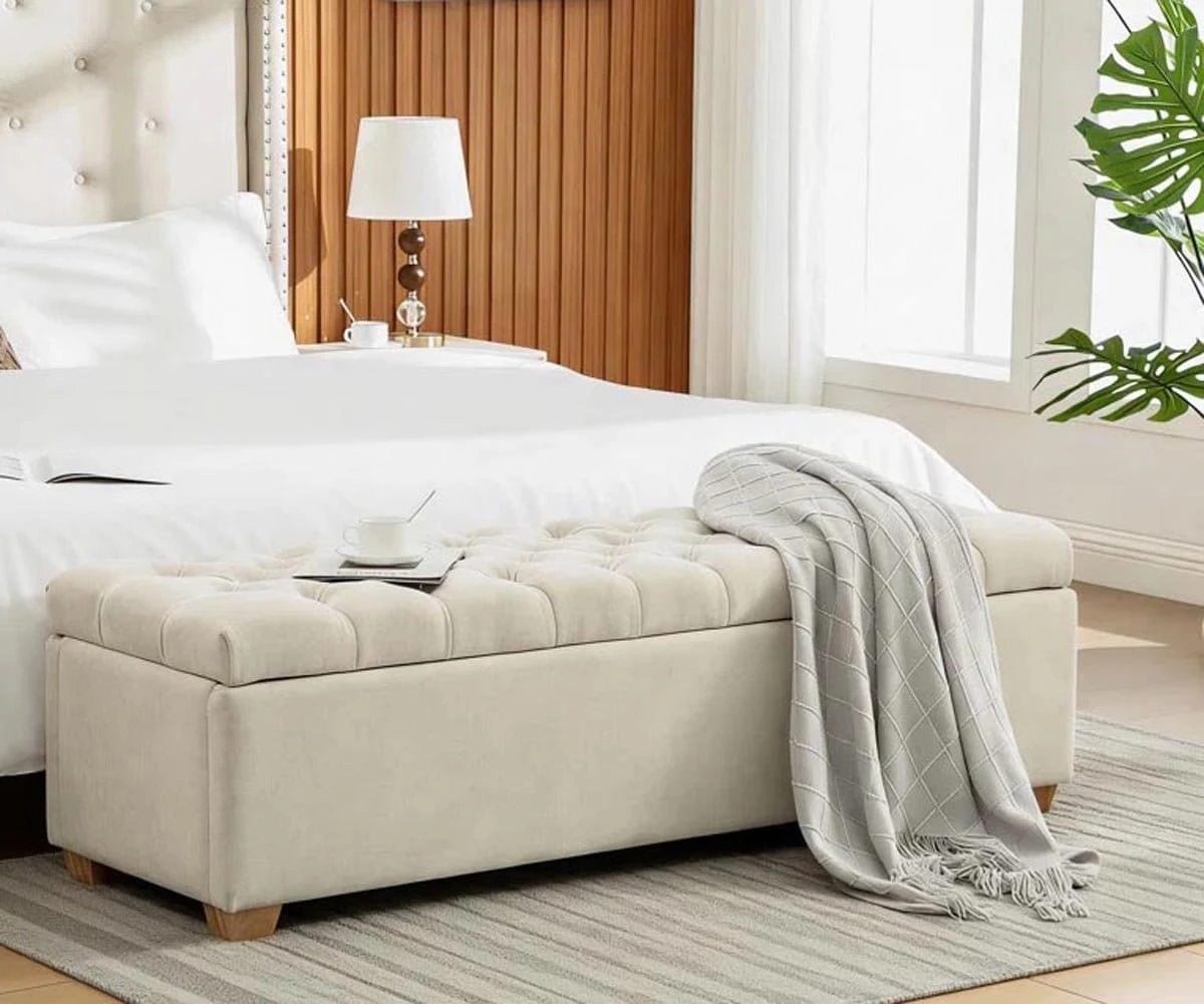 Beige tufted bench styled at the foot of a bed with a draped throw and tray on top
