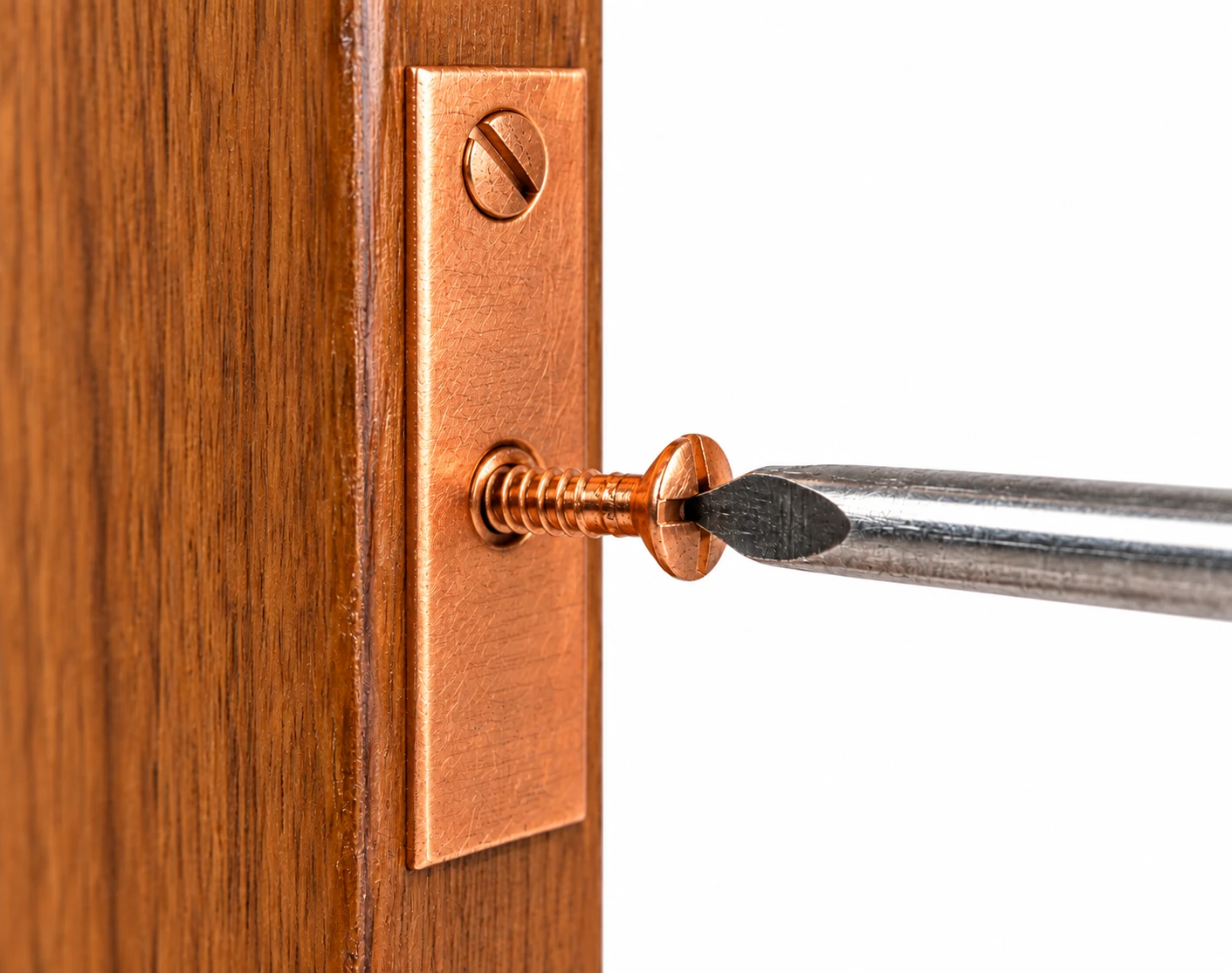 Copper slotted countersunk screw being tightened with a flathead screwdriver into a copper plate on wood