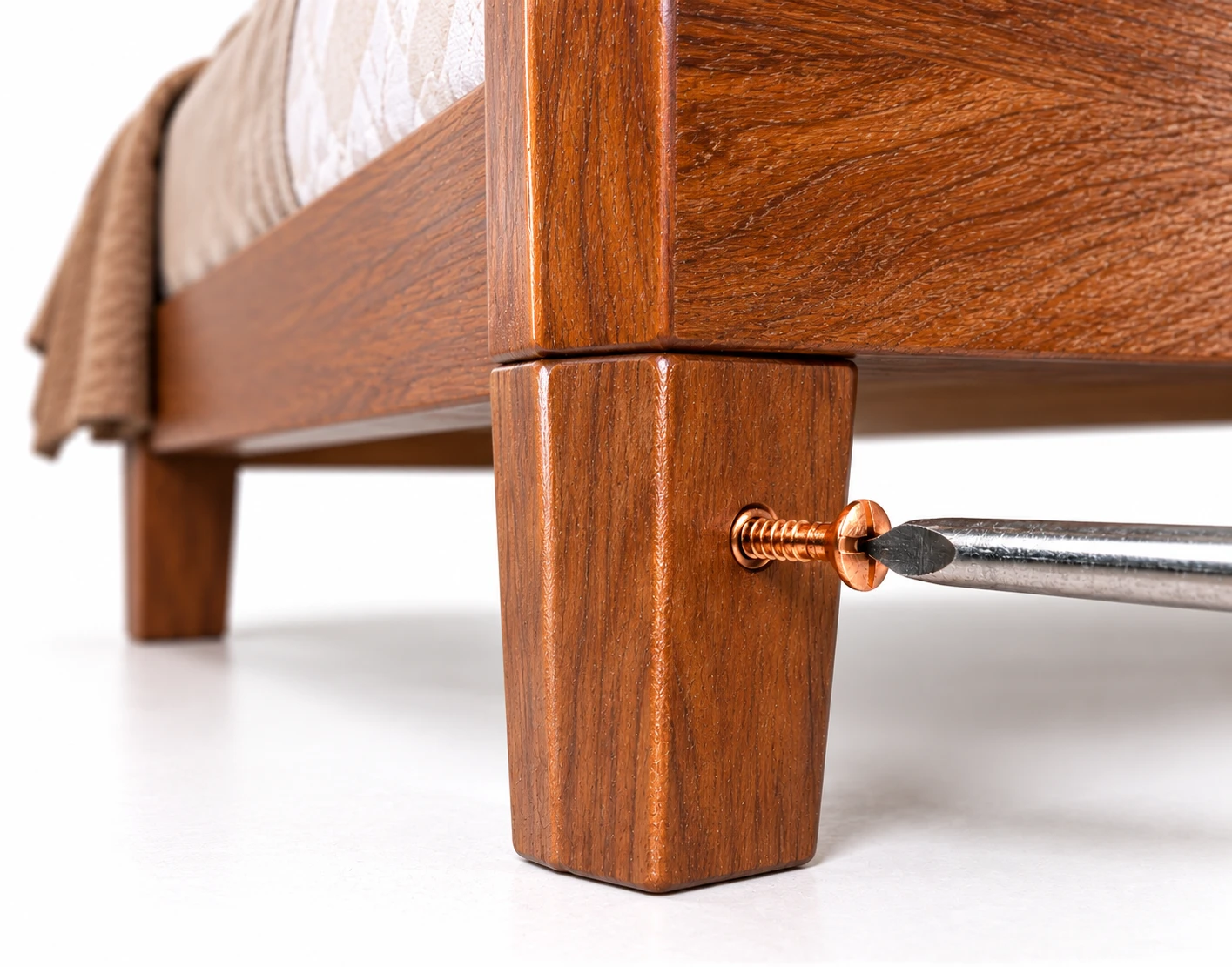 Close-up of a copper slotted countersunk screw being driven into a wooden bed leg with a flathead screwdriver