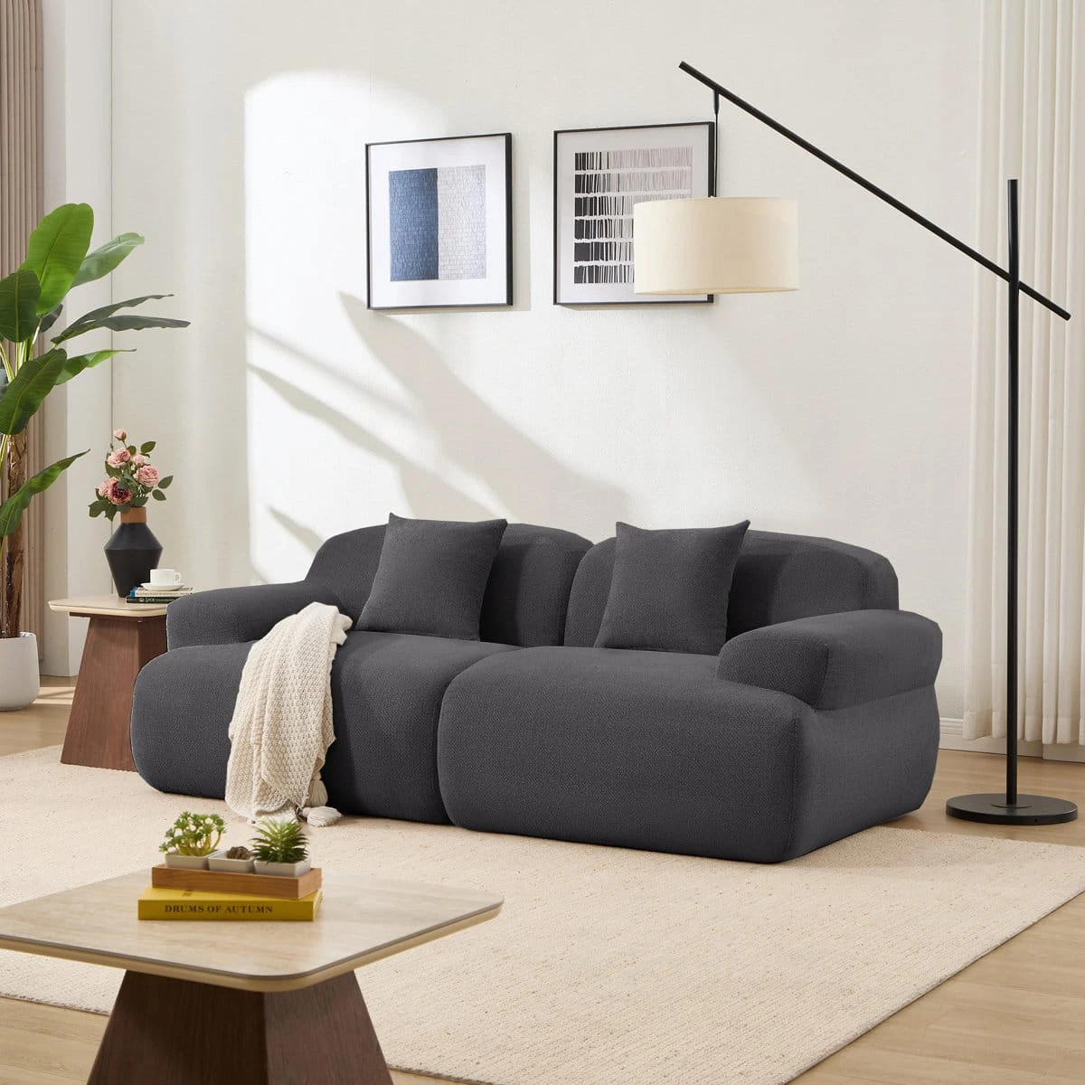 Three-seat dark grey curved sofa with ottoman styled in a bright living room with pillows and throw