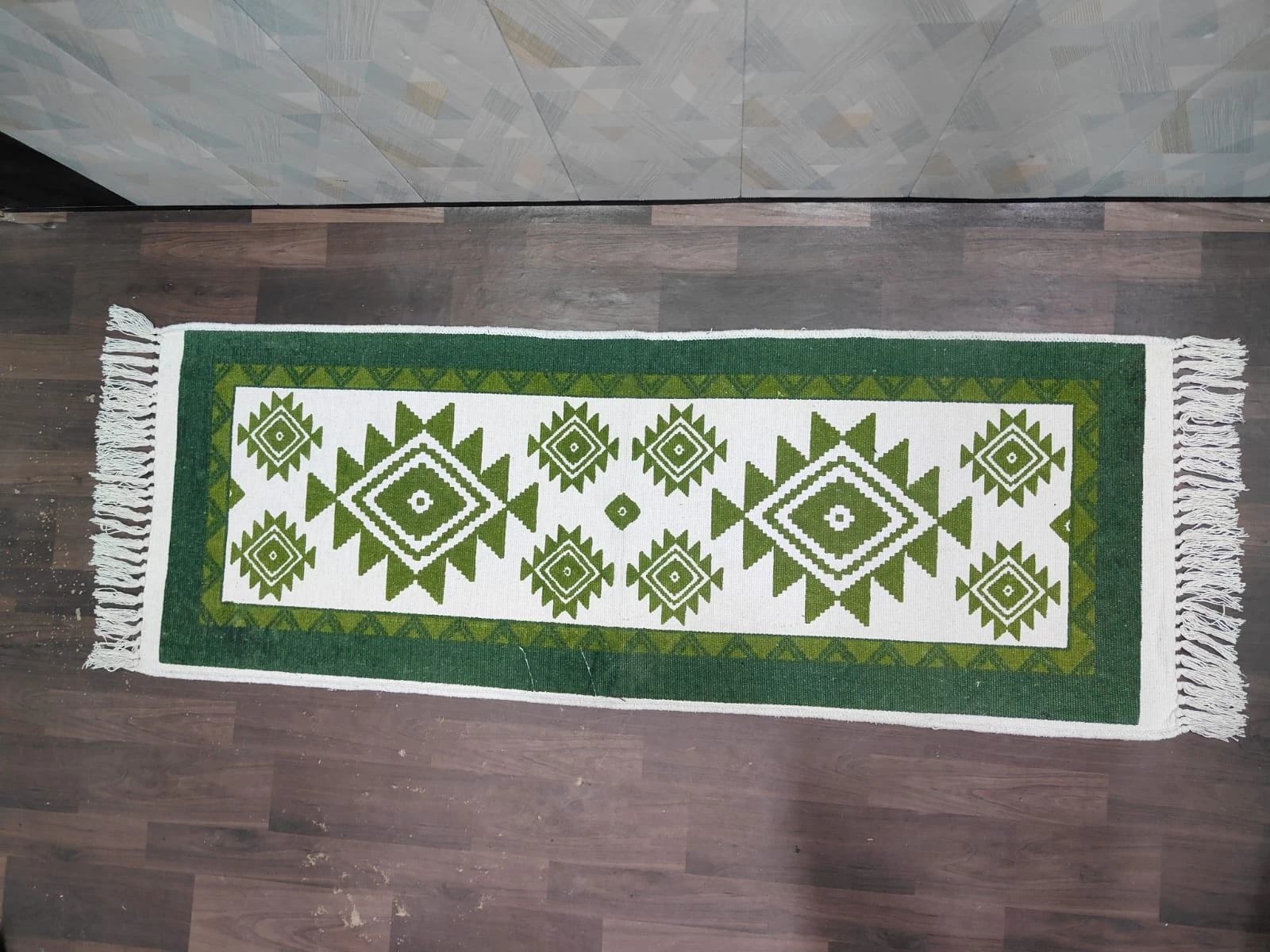 Top view of green and white runner rug with diamond motifs, dark green border, and fringe on both ends