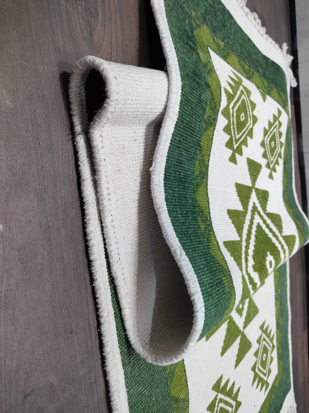 Close-up of the folded rug showing cream underside, bound edge, and green geometric pattern