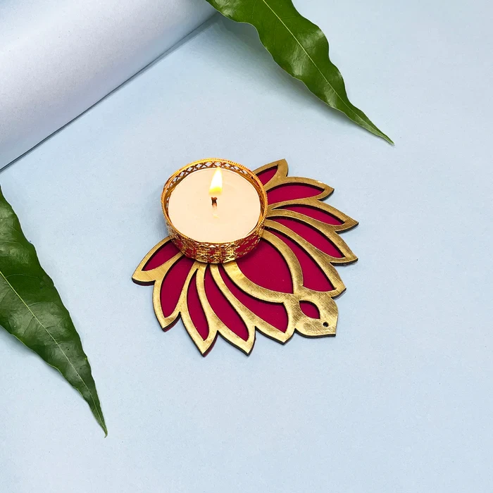 Lit tealight in ornate gold cup on a pink and gold lotus-shaped base, styled flat with green leaves