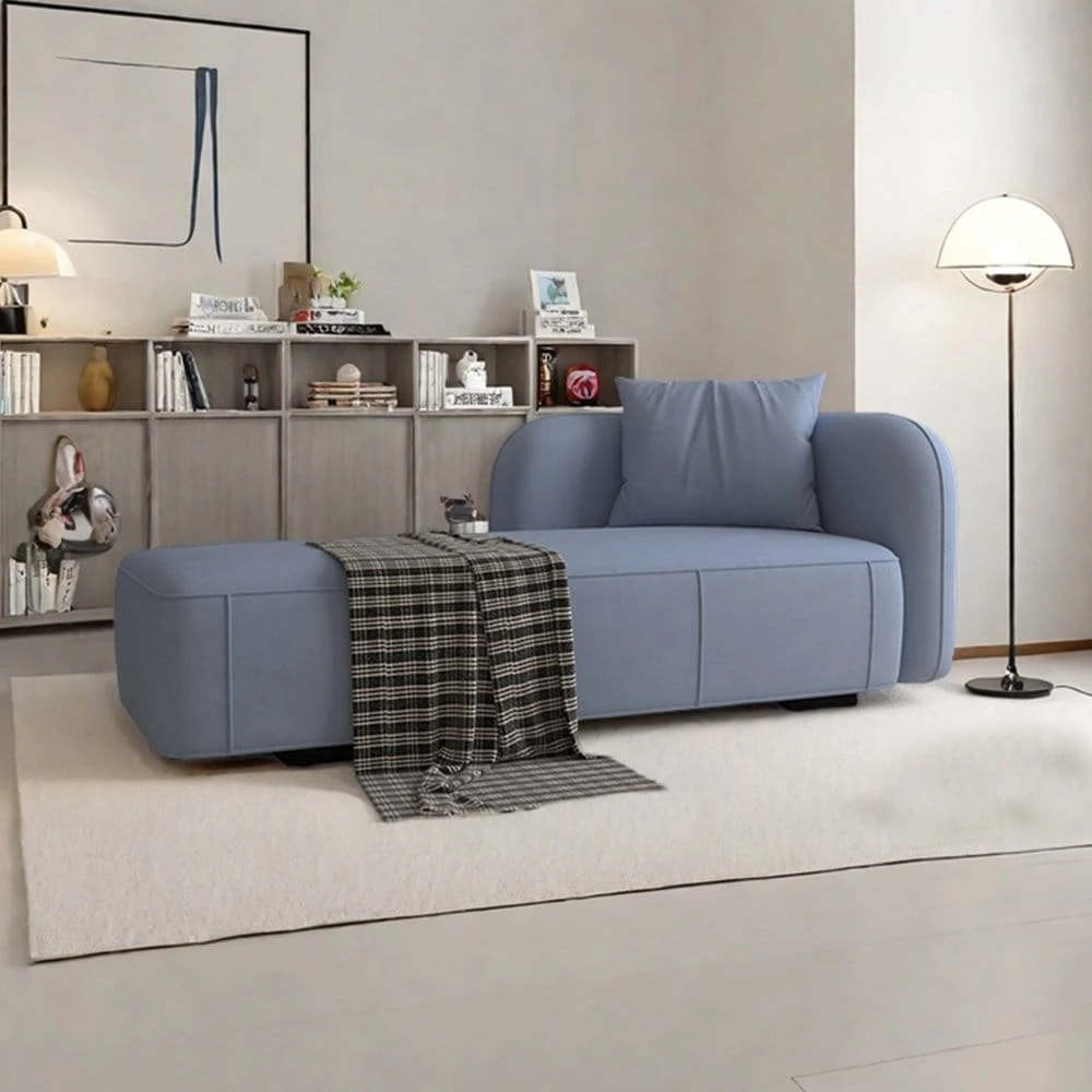 Blue upholstered chaise lounge sofa with rounded armrest, matching cushion, and plaid throw in a styled living room