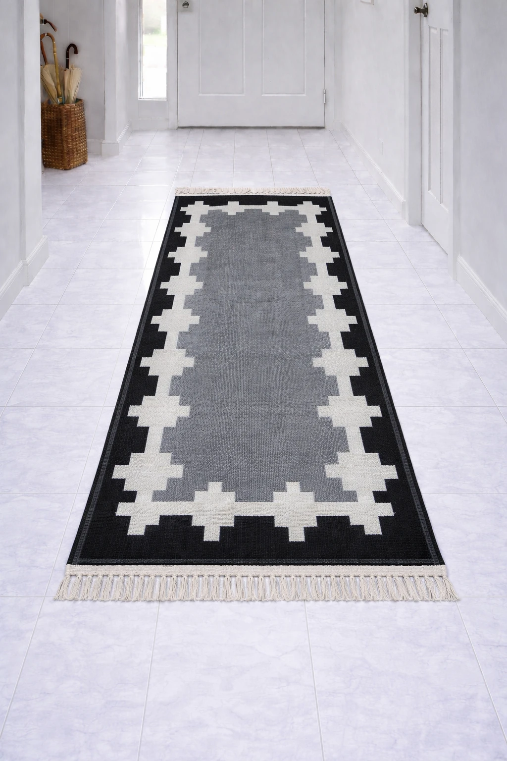 Geometric black, white and grey runner rug with tassel fringe laid lengthwise in a bright tiled hallway