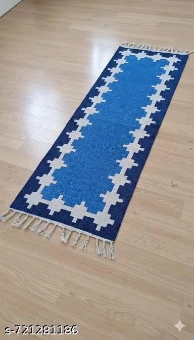 Narrow blue woven runner rug with white stepped border and tassels at both ends on a light wood floor
