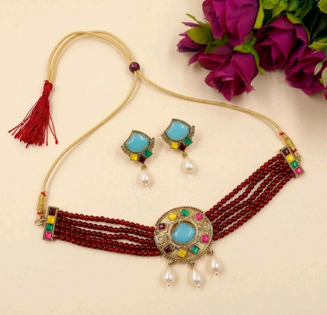 Flat lay of maroon five-strand beaded choker set with gold cord tie, tassel, matching blue-and-pearl earrings