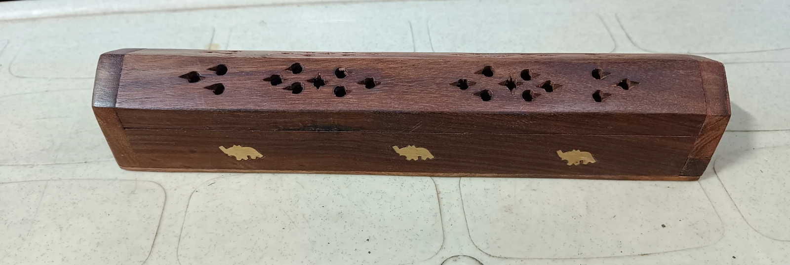 Rectangular dark wood incense box with floral cutout lid and three brass elephant inlays along the side