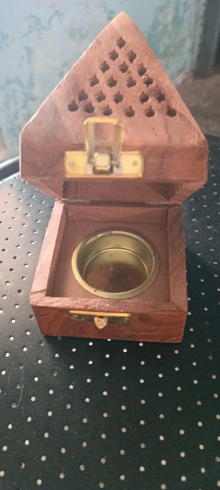Open wooden incense box angled upward, showing brass inner cup, top latch, and vent holes in the raised lid