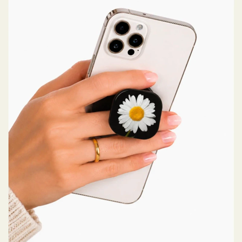 Close-up of black square phone grip with white daisy design attached to a silver smartphone