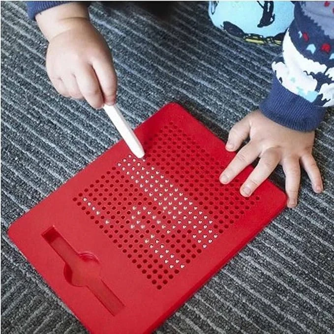 Toddler using white stylus on a red magnetic dot drawing board placed on a gray carpet