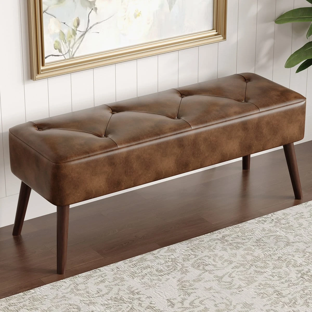 Brown upholstered bench on wood flooring, showing the tufted top and tapered dark wood legs