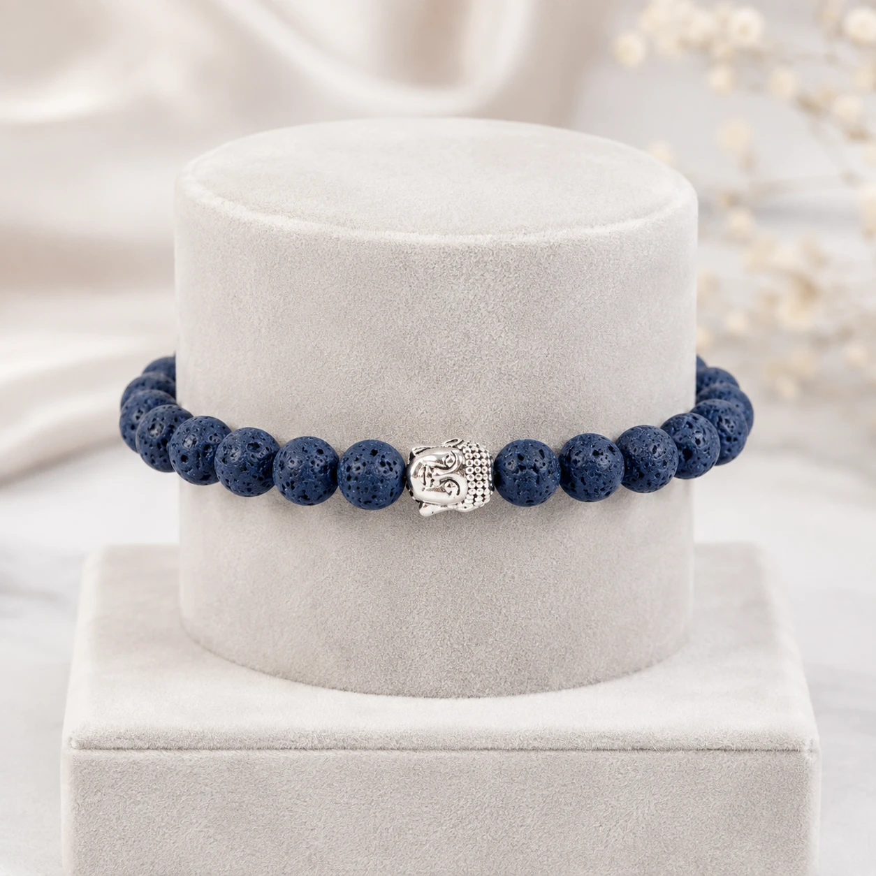 Blue lava bead stretch bracelet with silver Buddha accent on a cream stand in a soft light setting