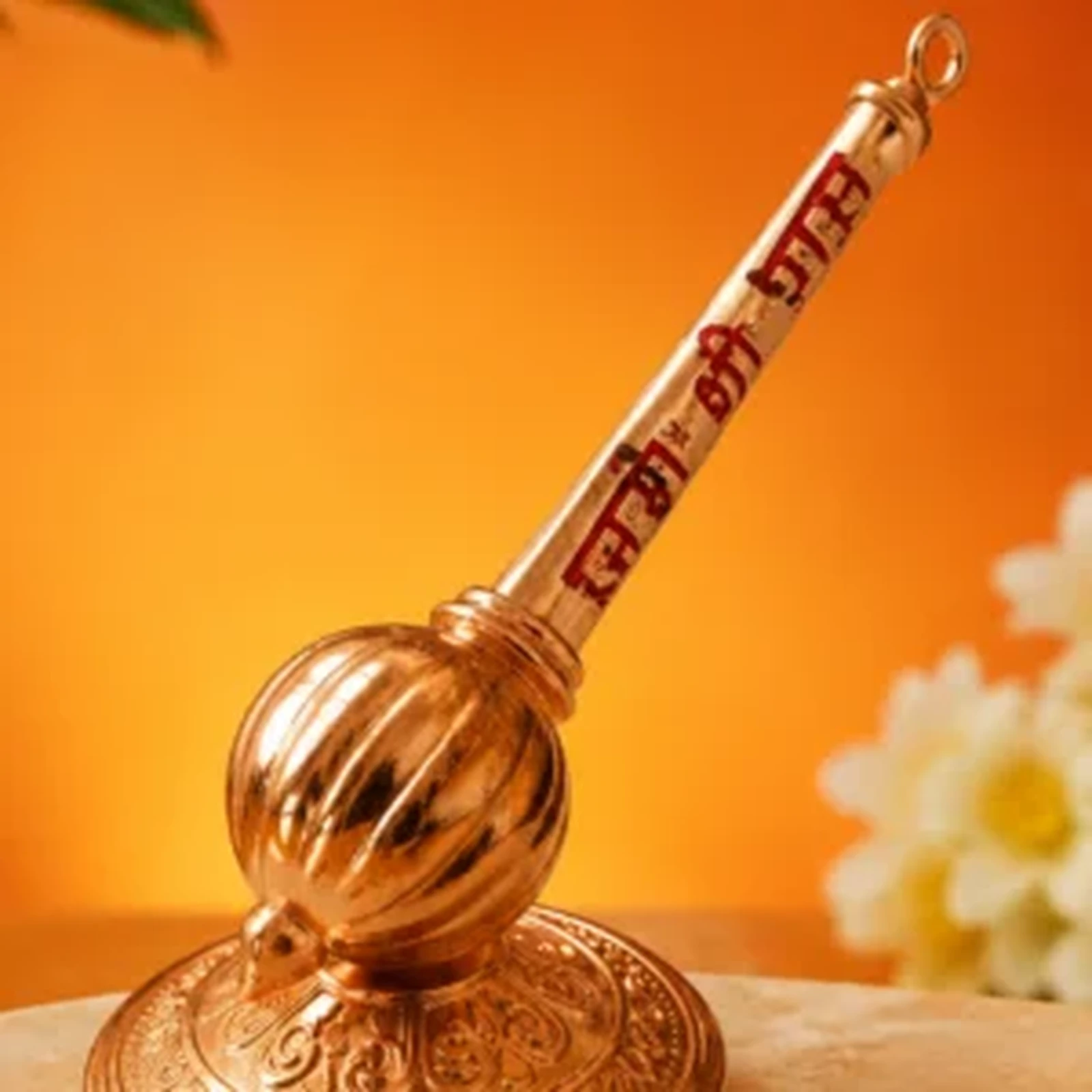 Copper-finish pooja bell lying on its side, showing ribbed dome and red script on the handle