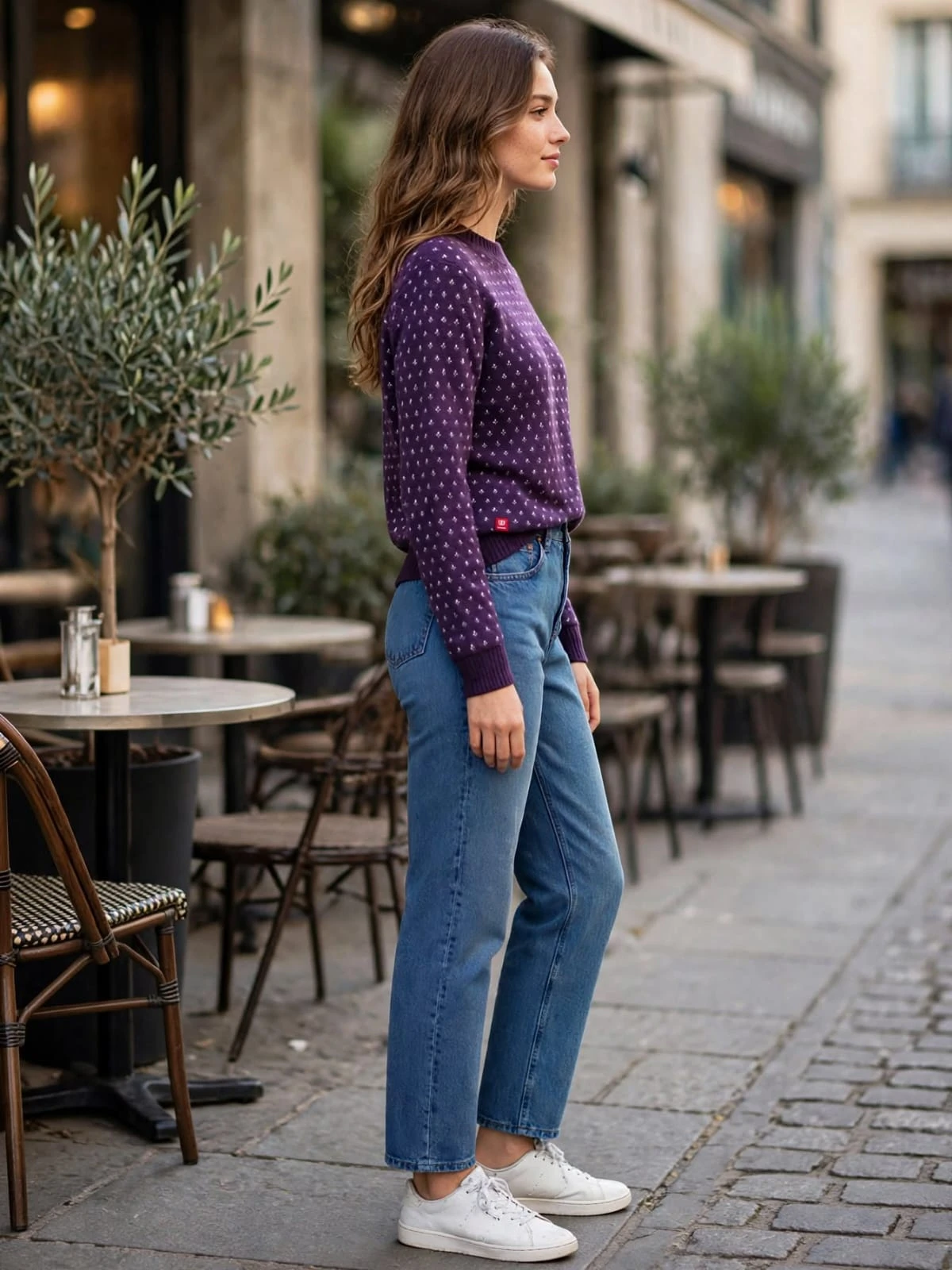 Side profile of the purple patterned crewneck sweater tucked into straight-leg blue jeans on a city sidewalk