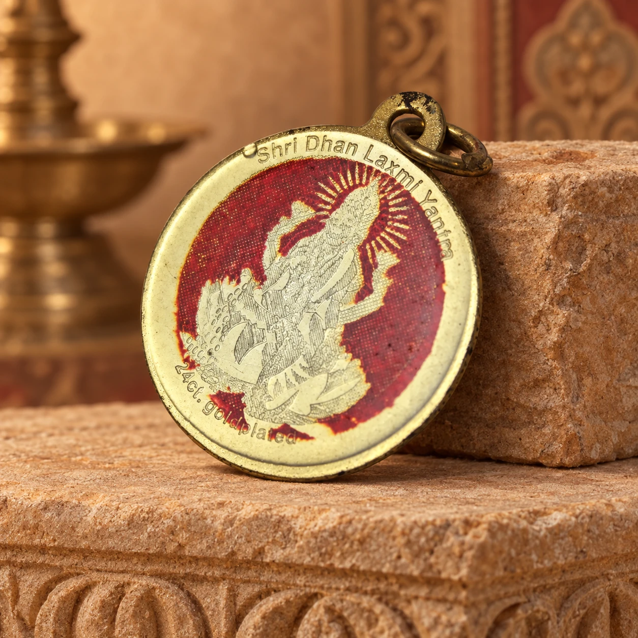 Back side of the round pendant with worn red deity print, hanging loop, and 24ct gold plated text