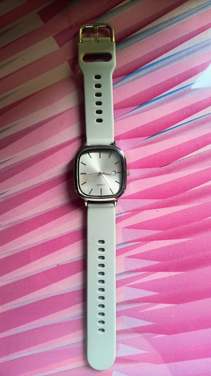 Watch laid flat with square silver-tone case, sunray dial and pale strap on a pink striped surface