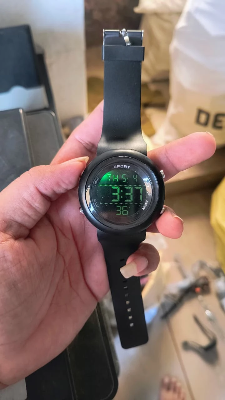Front view of black digital sport watch in hand, green display lit and buckle strap extended