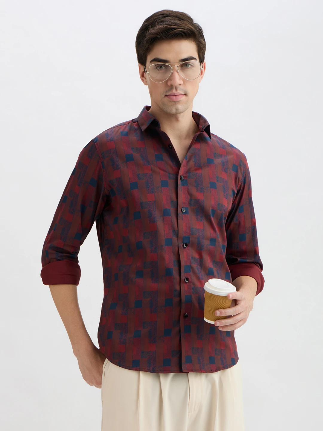 Three-quarter front view of the shirt with rolled cuffs and geometric print, styled holding a coffee cup