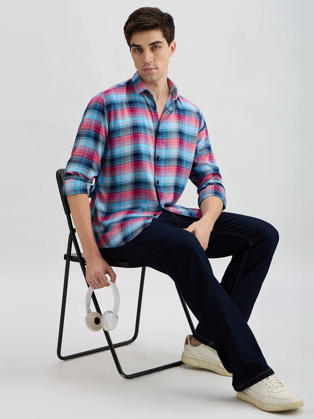 Seated styling view of the checked shirt paired with dark jeans and white sneakers