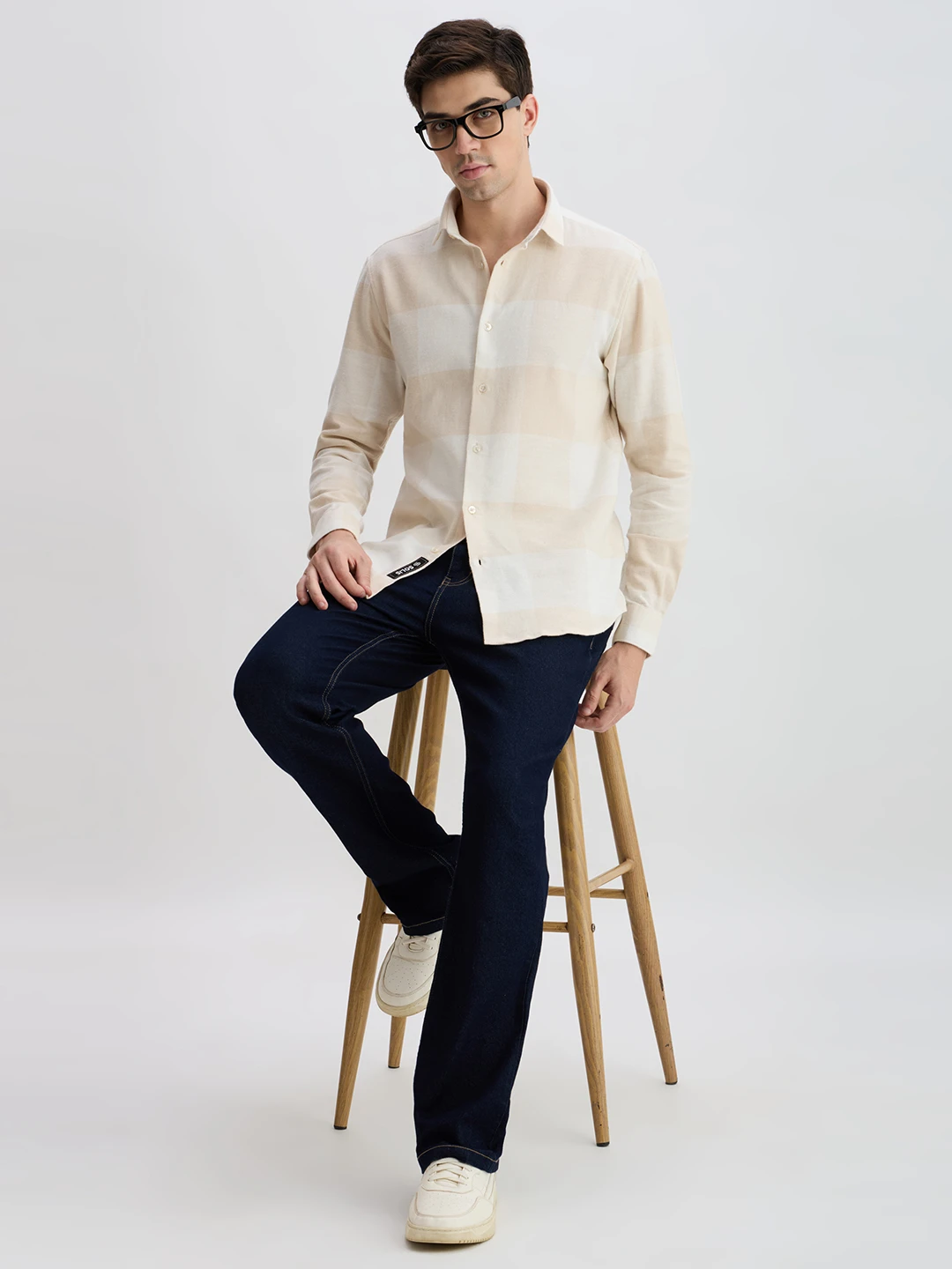 Full-body styled view with the shirt worn open at the hem while seated on a wooden stool