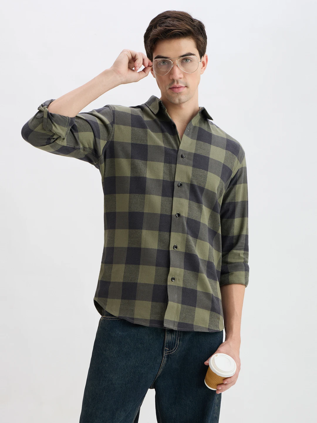 Model wearing olive and charcoal buffalo check shirt with rolled sleeves, adjusting glasses