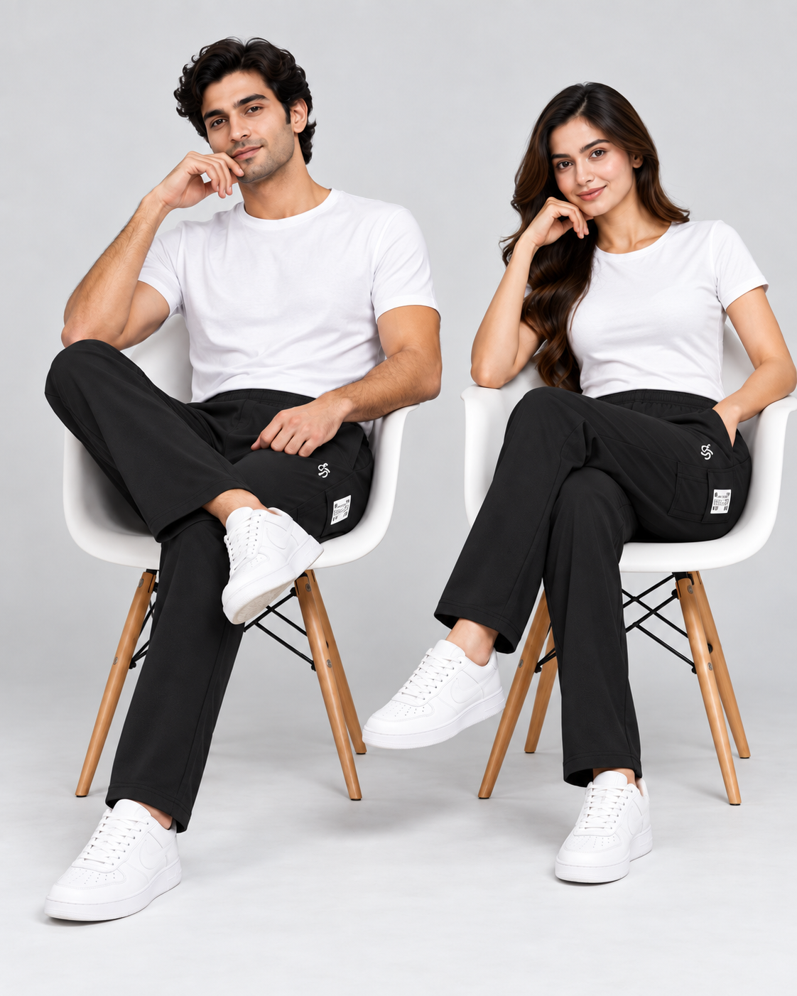 Seated male and female models styling the black track pants with white tops and sneakers