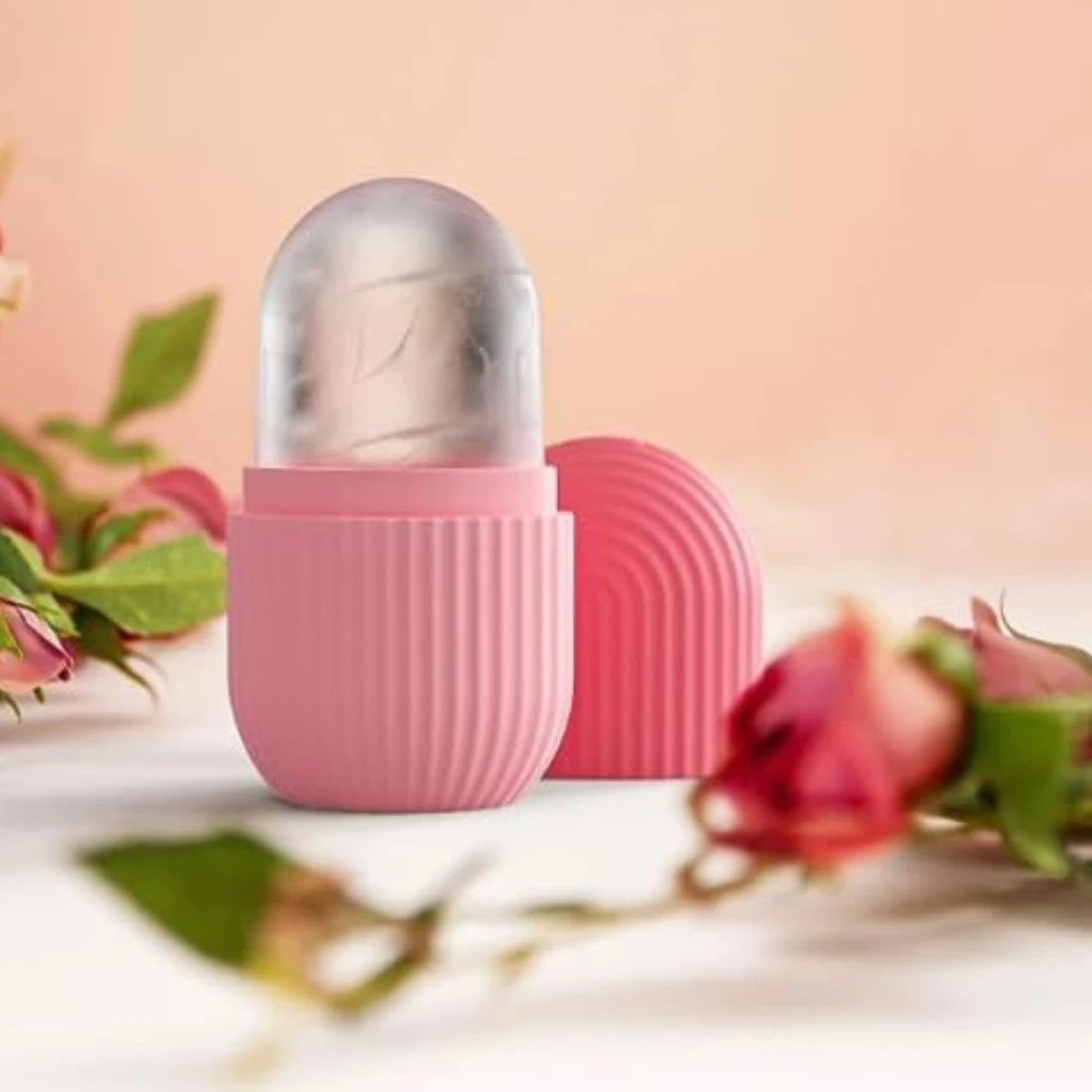 Open pink silicone ice roller with frosted head and cap set behind on a rose-styled surface