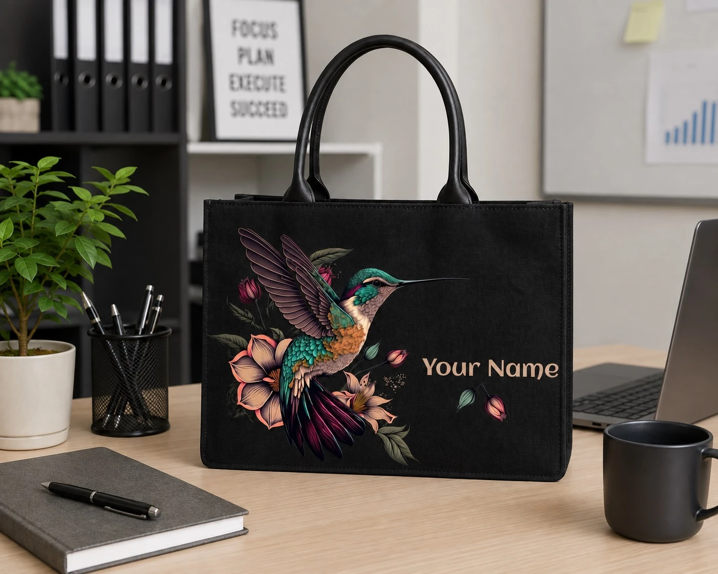 Black personalized tote bag displayed on an office desk beside laptop, mug, notebook and pen holder